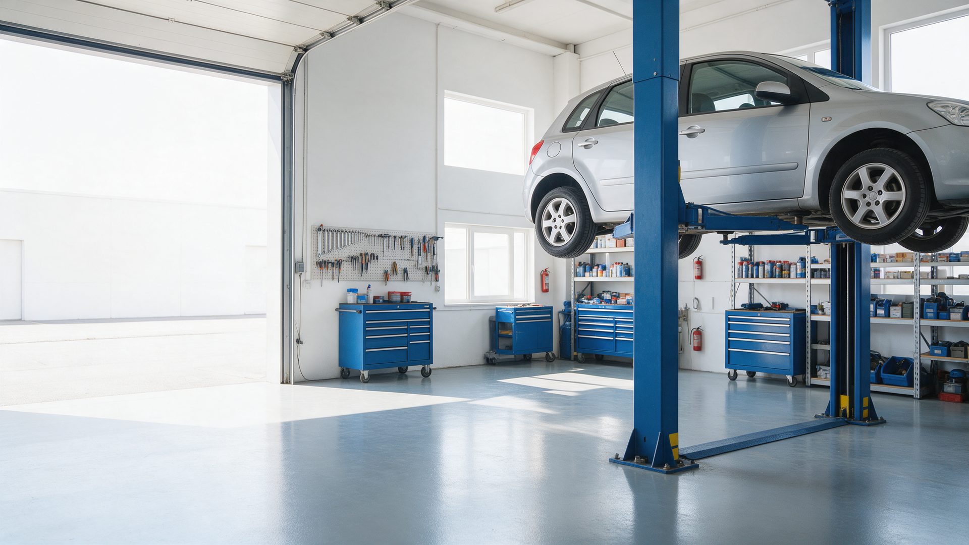 A silver hatchback raised on a blue two-post lift in a bright, tidy workshop